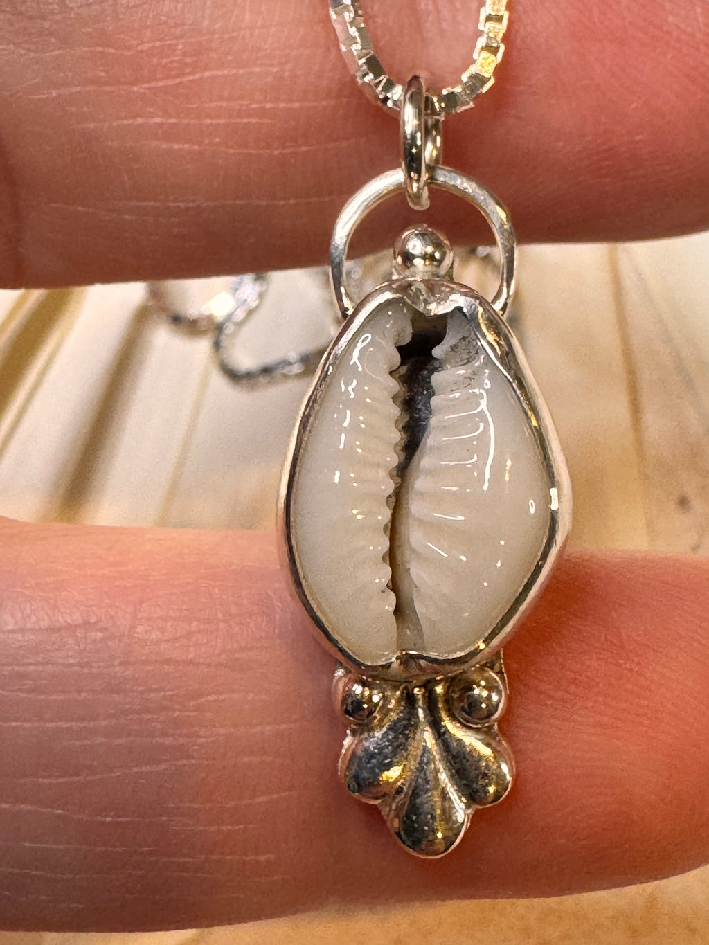 silver pendant with a shell charm on a finger against a neutral background
