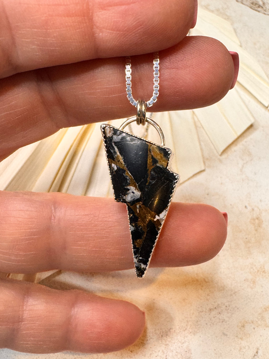 Hand holding a necklace with a white buffalo lightning bolt pendant against a neutral background