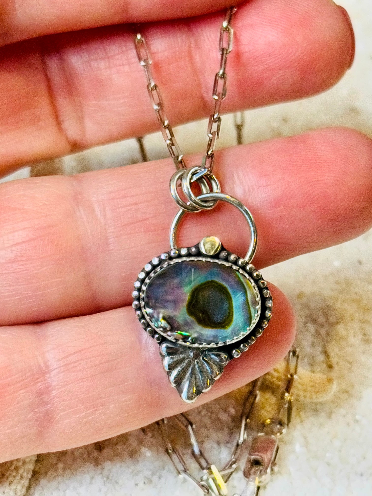 Abalone Necklace with a pendant held between fingers on a neutral background