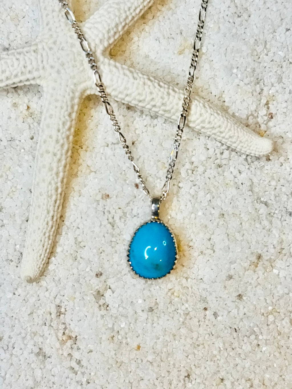 Tear drop shaped Bisbee turquoise anklet on a silver Figaro chain against a sandy background