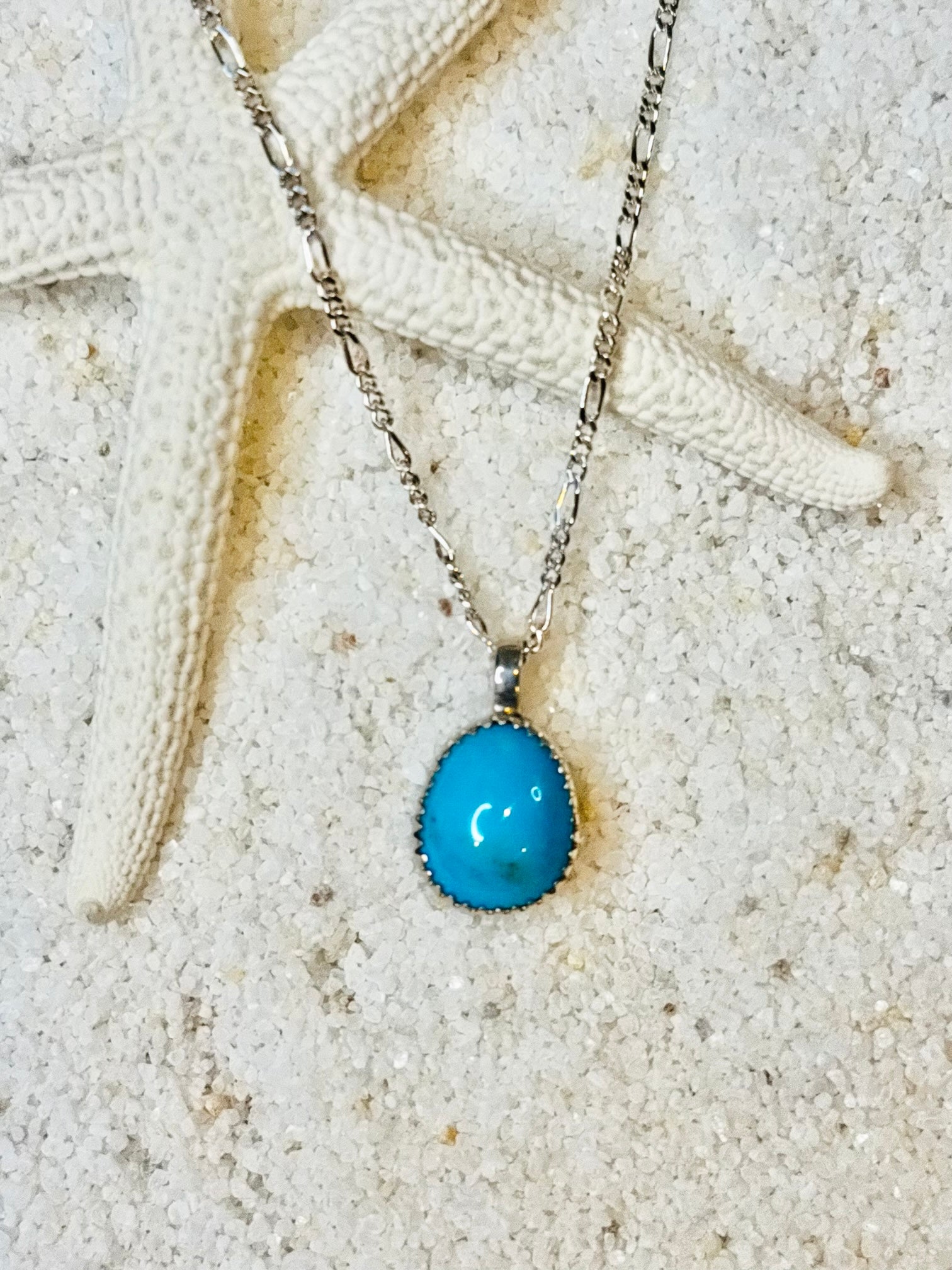 Tear drop shaped Bisbee turquoise anklet on a silver Figaro chain against a sandy background