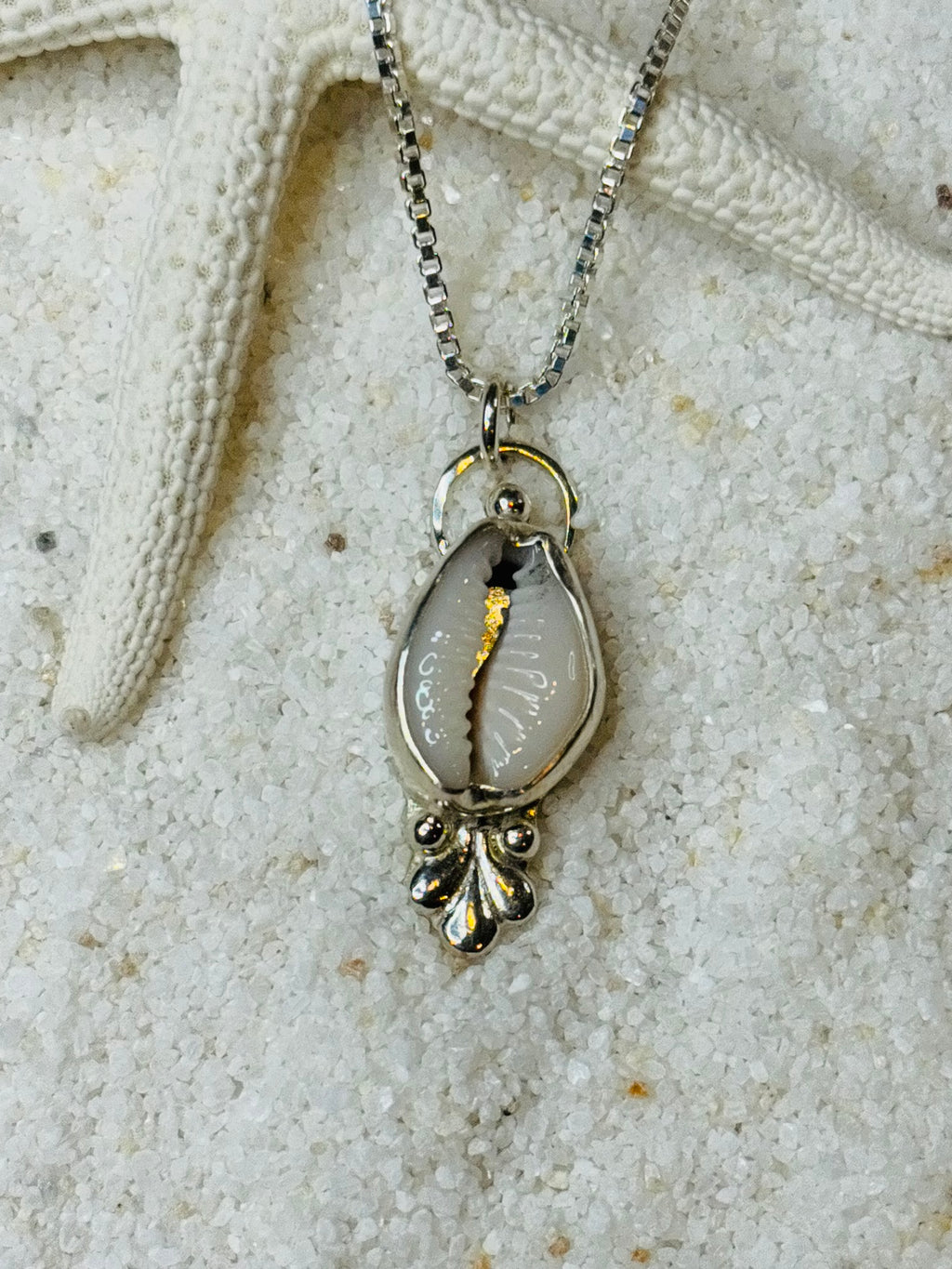 Silver necklace with a cowrie shell pendant on a sandy background