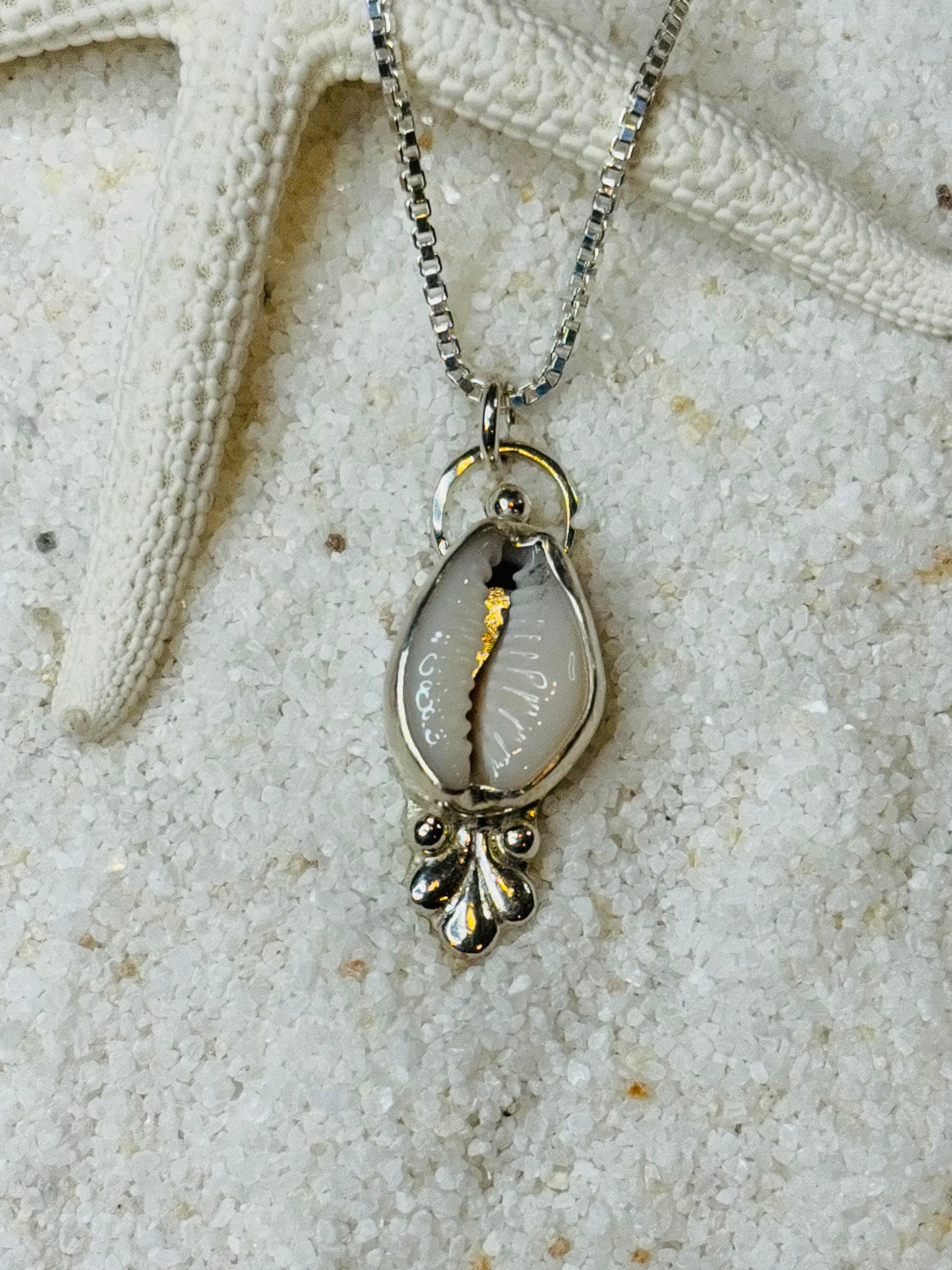 Silver necklace with a cowrie shell pendant on a sandy background