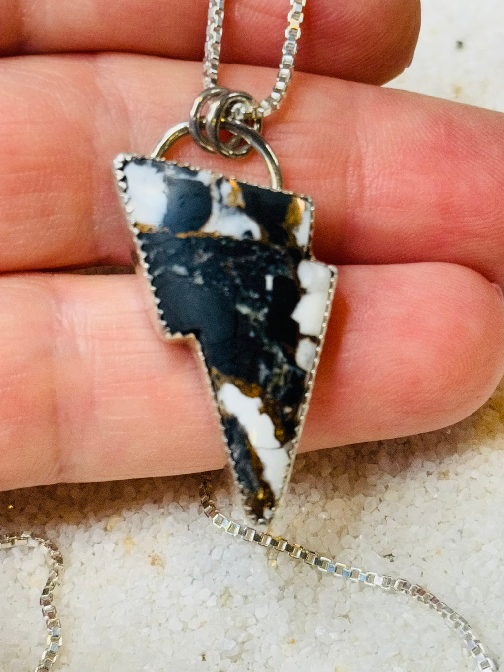 Necklace with a unique pendant held between fingers on a neutral background