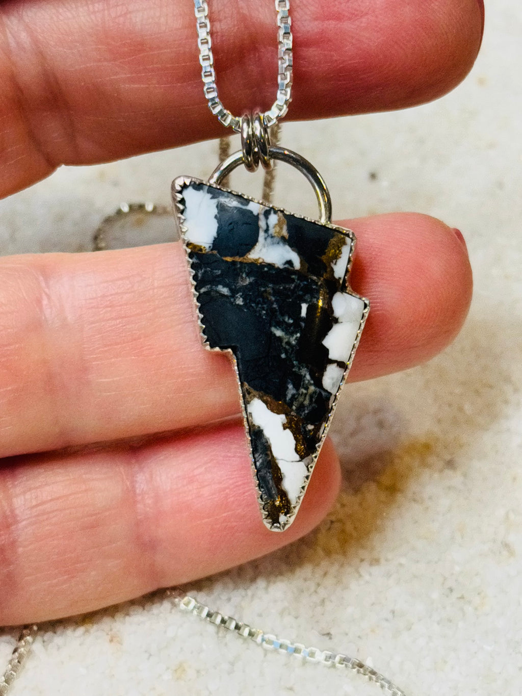 Necklace with a lightning bolt pendant held between fingers on a neutral background