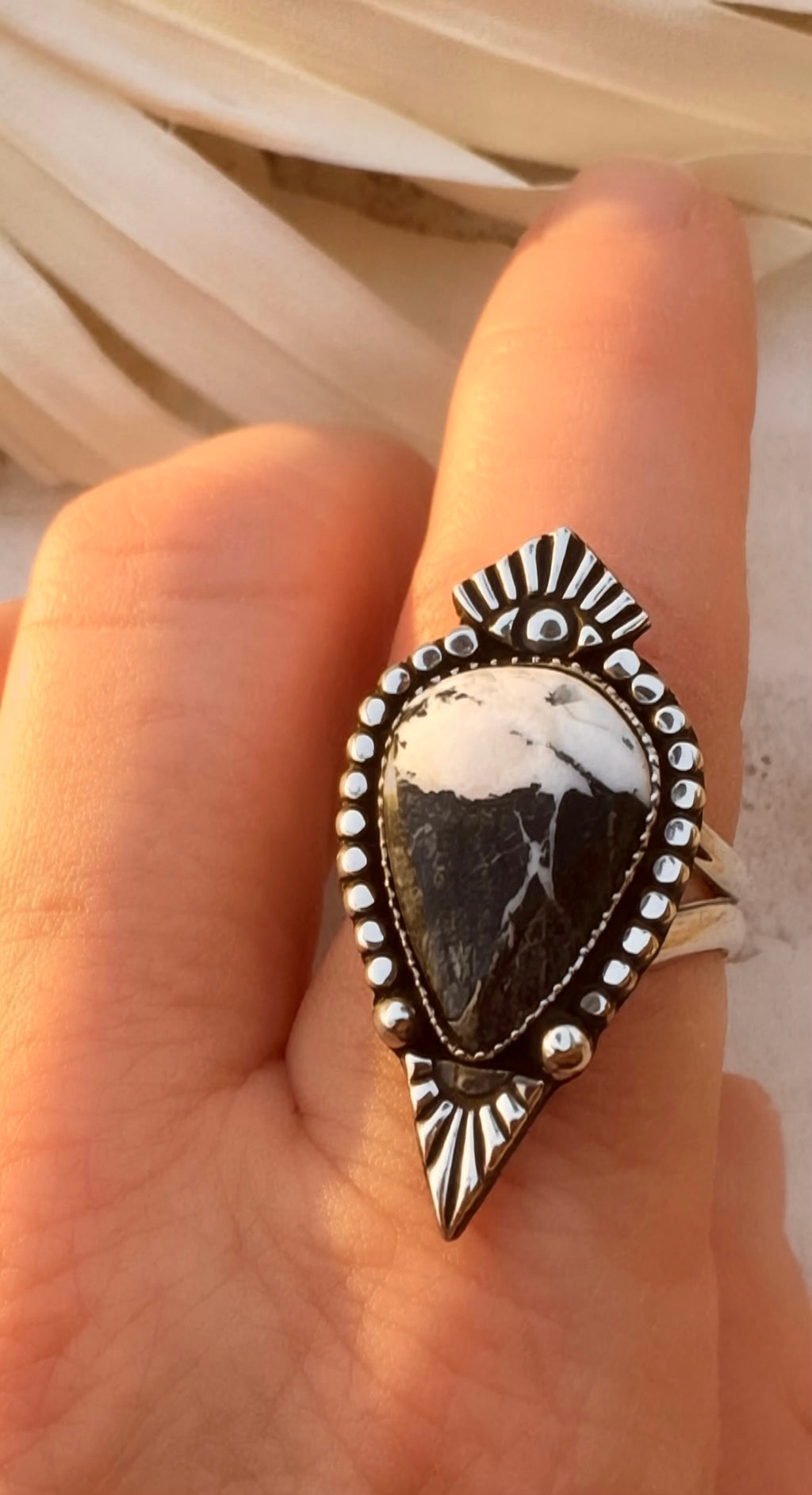 Silver ring with a large white buffalo stone on a hand against a neutral background