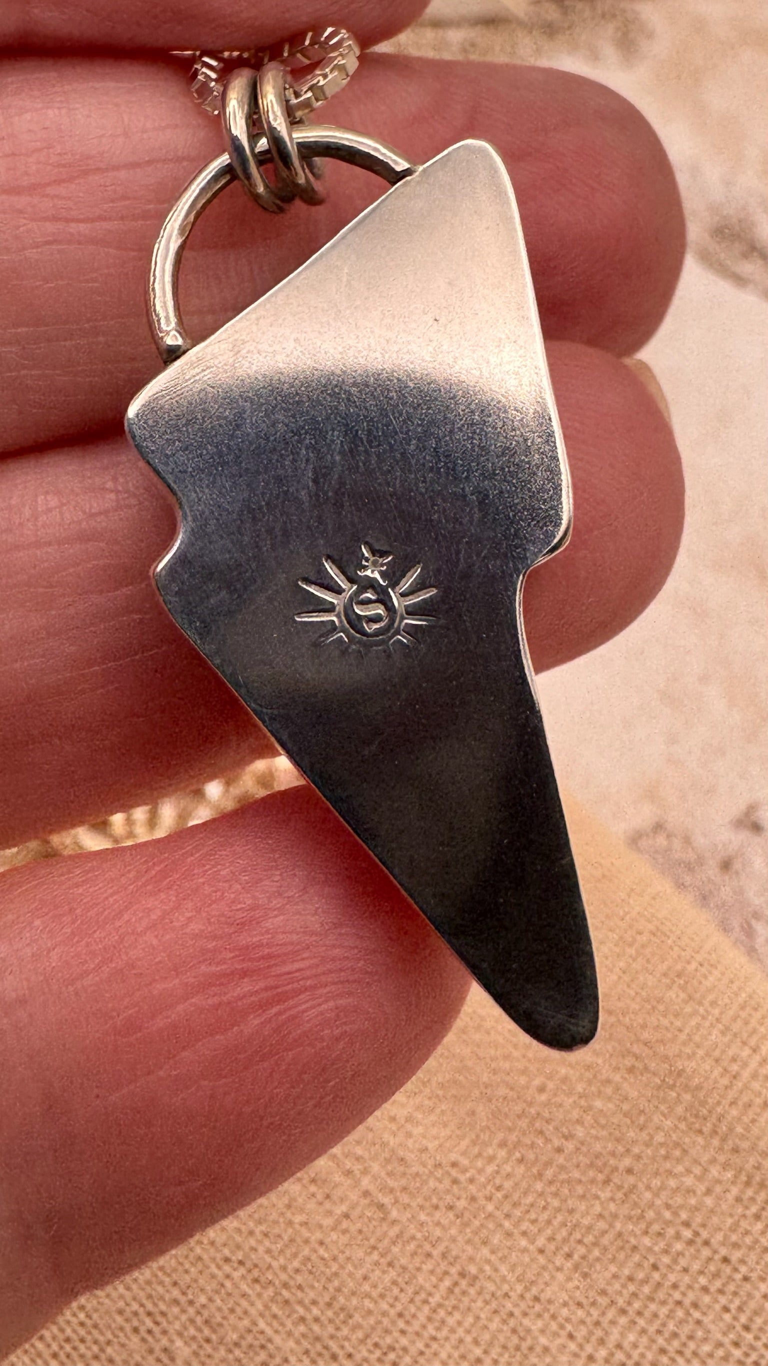 Silver lightning bolt-shaped pendant with a logo held between fingers.
