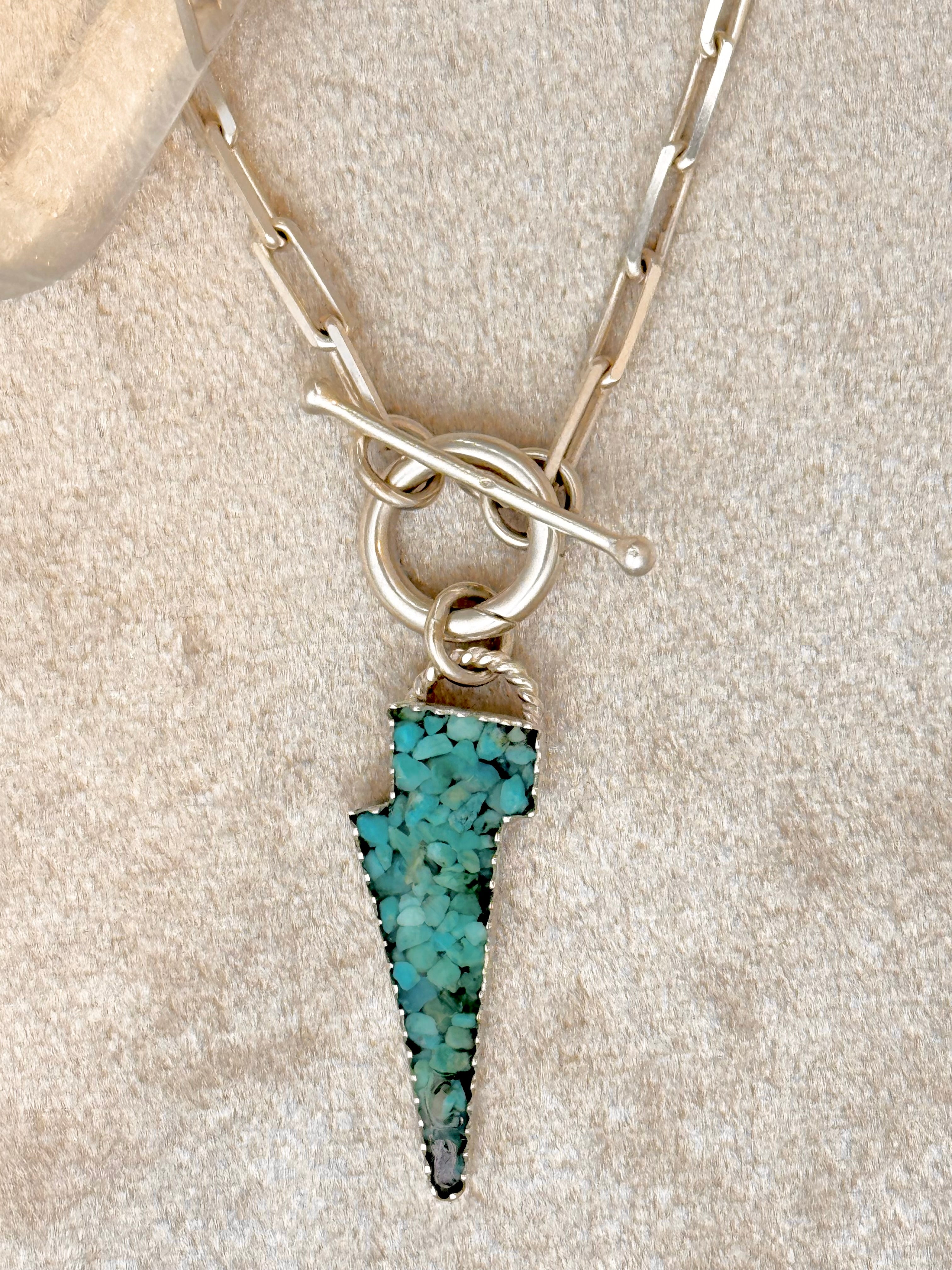 Lightning bolt pendant with Kingman turquoise inlay on a paperclip toggle chain, against a crème background. 