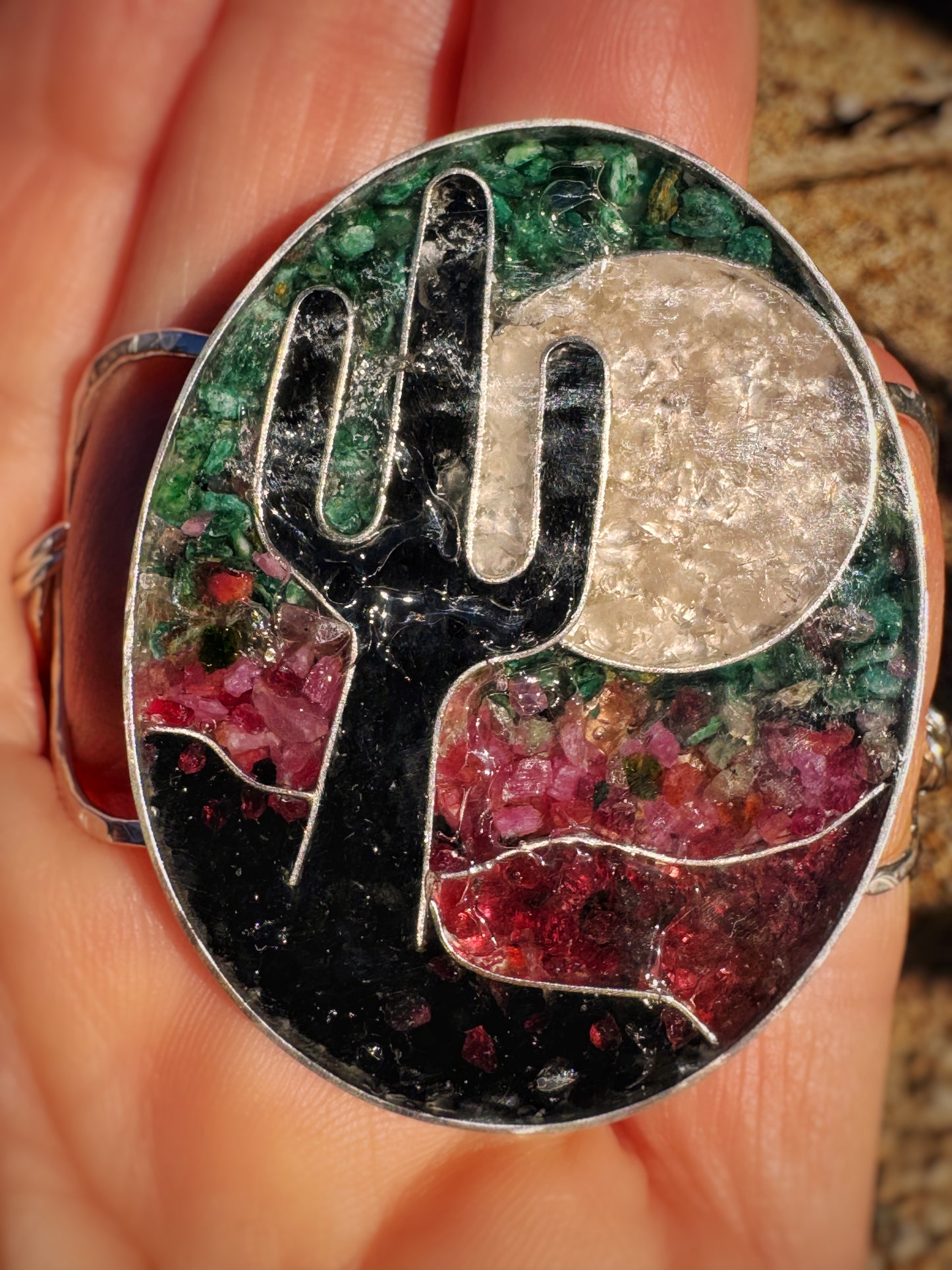 Silver cuff with a cactus design and inlay gems and minerals held in a hand.