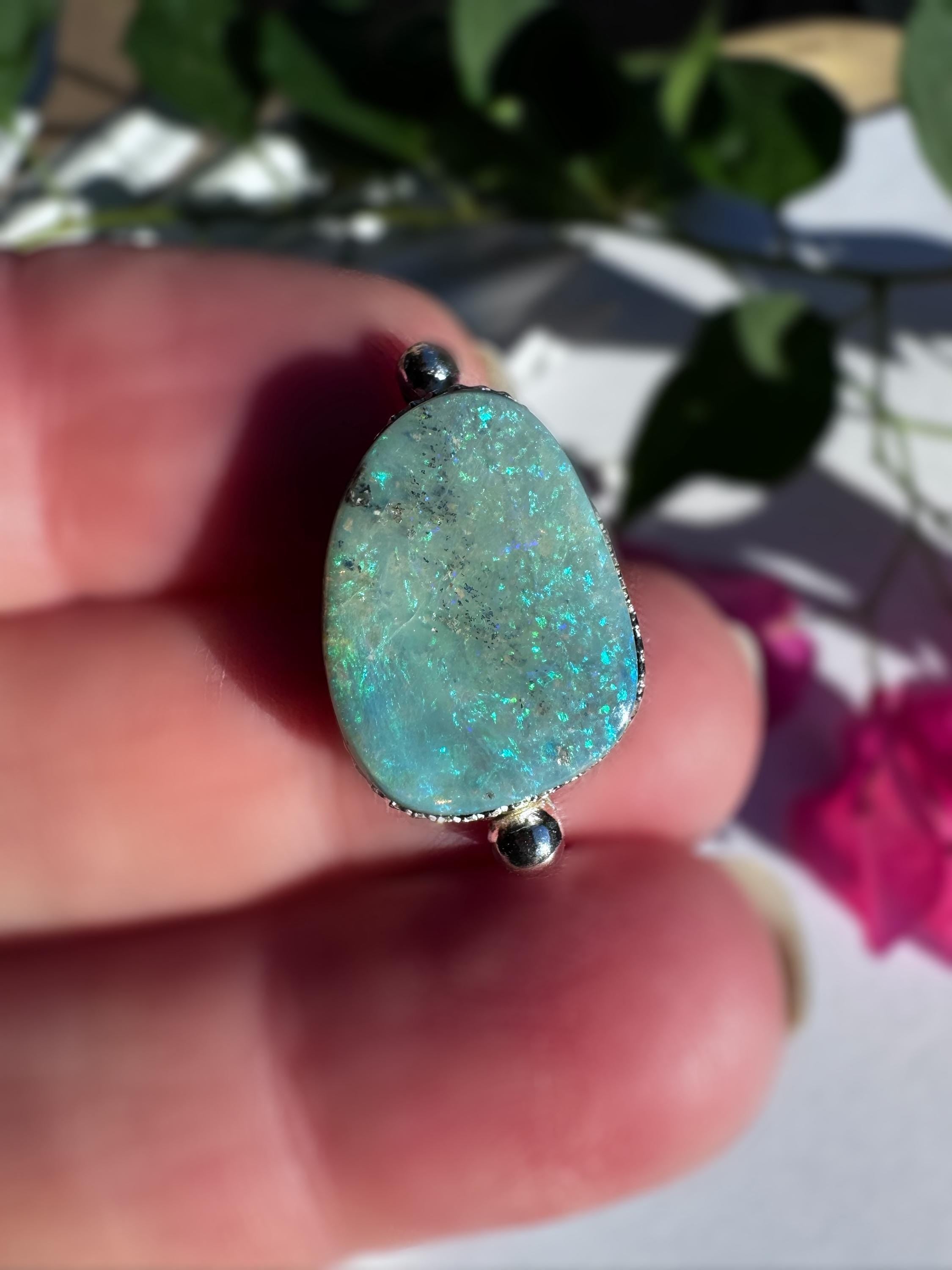 Ring with an opal held in a hand against a blurred natural background